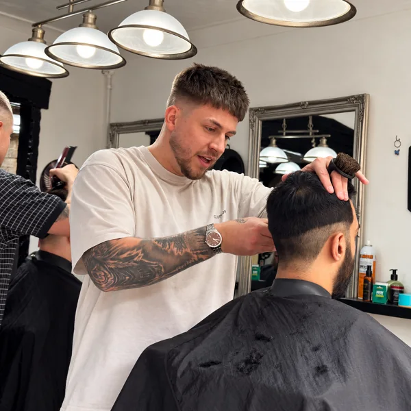 A barber at RAGE carefully shaping a client’s haircut