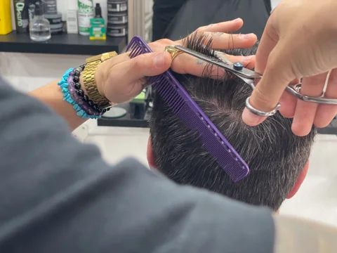 Close-up of a RAGE barber cutting hair with scissors and a comb