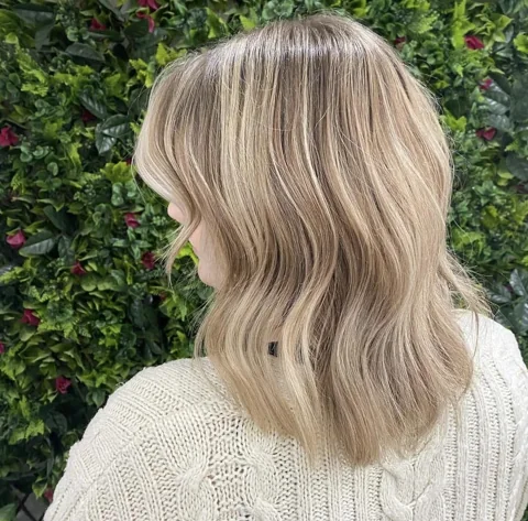 Soft blonde waves photographed against the salon’s floral wall